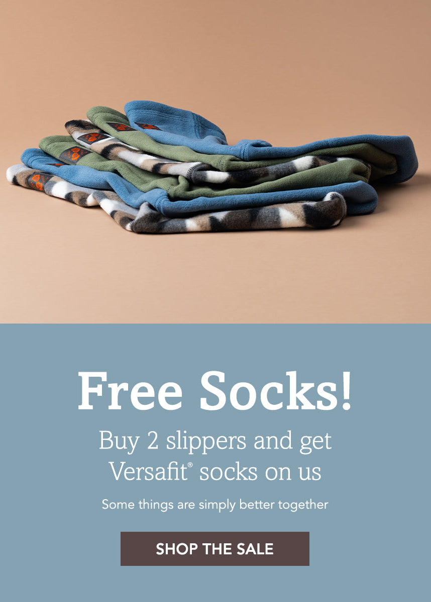 A promotional banner featuring a stack of folded Versafit socks in various patterns and colors on a warm beige background, with a blue-gray lower section containing text that reads 'Free Socks! Buy 2 slippers and get Versafit socks on us' and a 'SHOP THE SALE' button.