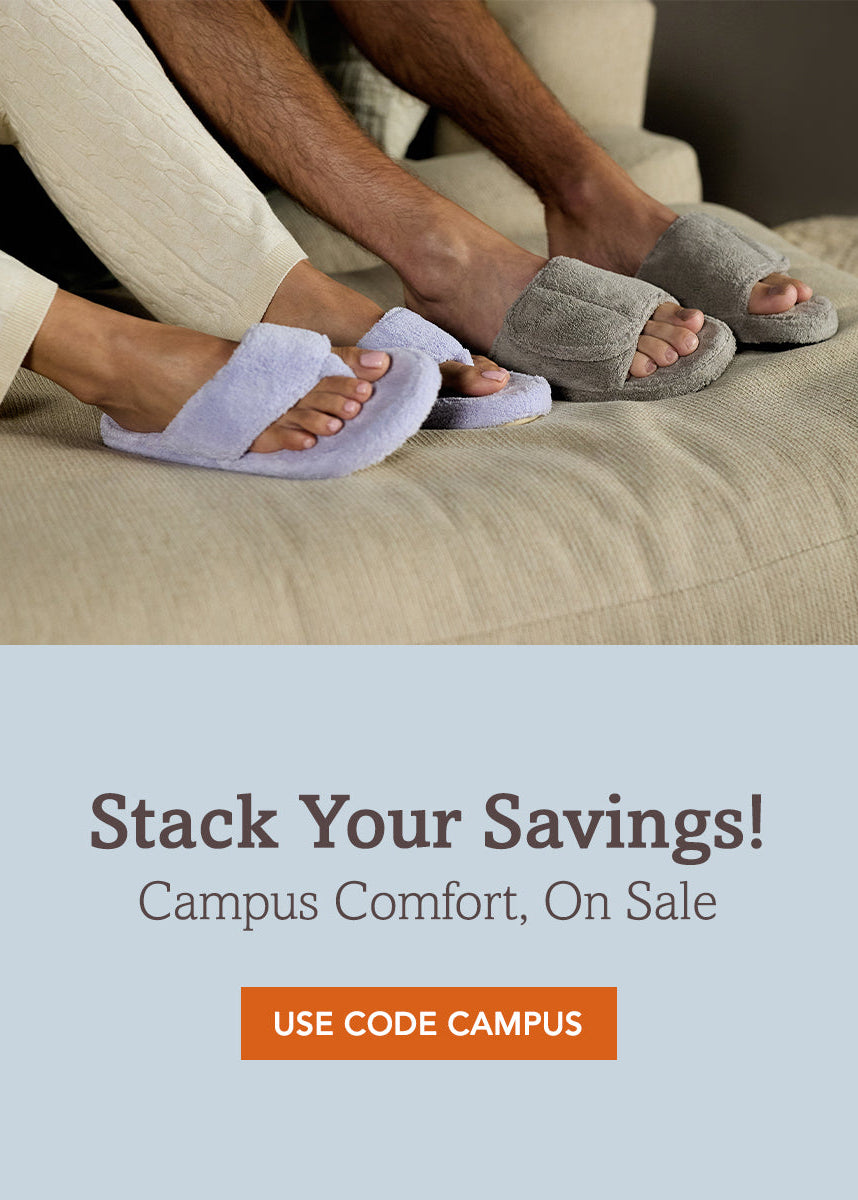 A promotional banner showing a person sitting on a beige couch wearing light lavender fuzzy slide slippers, with additional gray slide slippers on bare feet. The lower half has a light blue background with the text 'Stack Your Savings! Campus Comfort, On Sale' and an orange button reading 'USE CODE CAMPUS'.