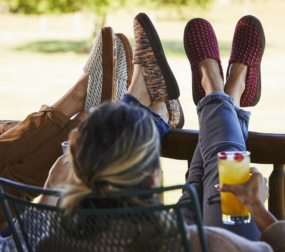 Women’s Original Acorn Moccasins in Ewe, Garnet and Sunset all on model with their feet up on the porch fence