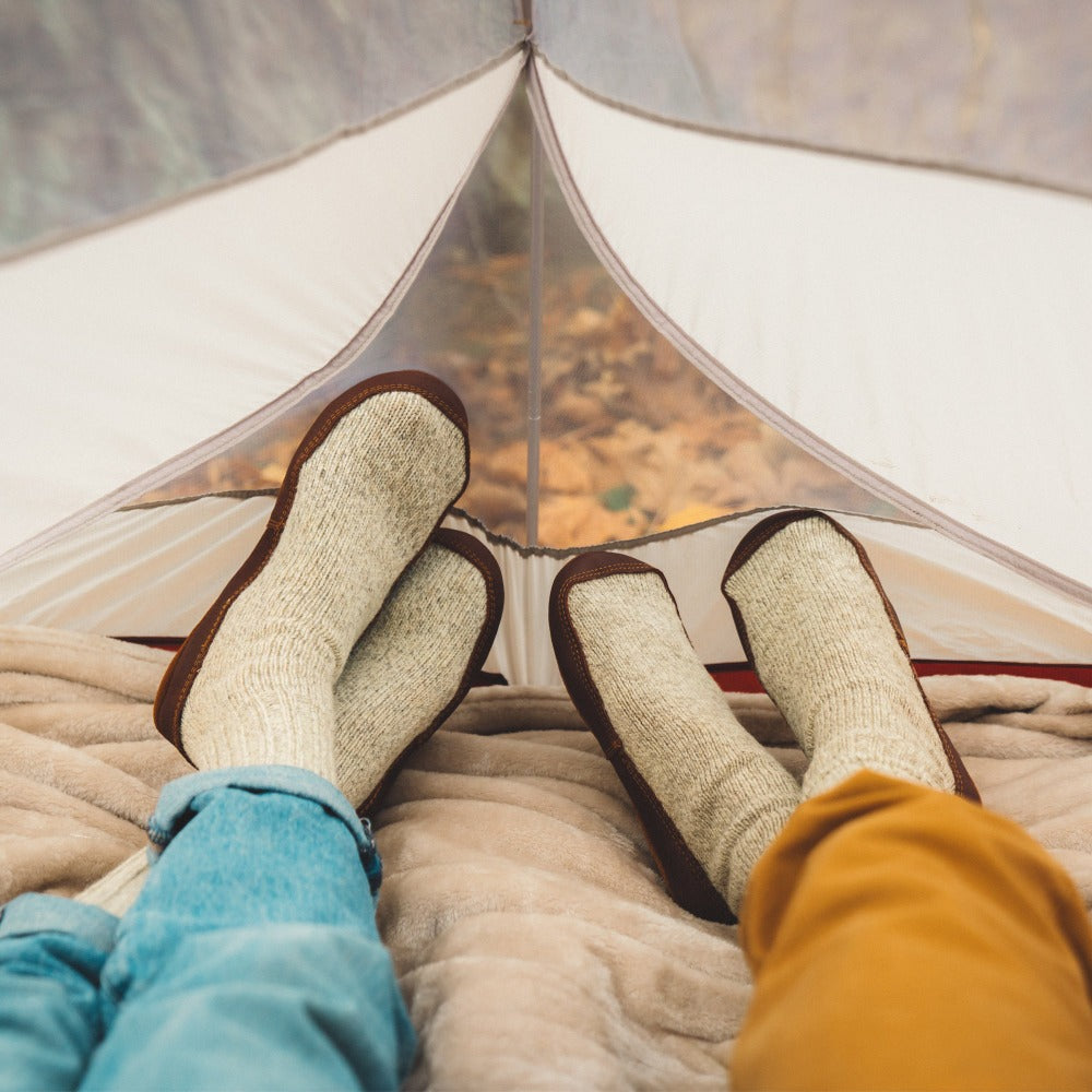 Male and Female model wearing the Acorn Slipper Sock in Grey Ragg Wool from the knee down while lounging in a tent
