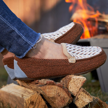 Women’s Andover Driver Moc Slipper in Buckskin sitting on a pile of wood with a campfire in the background