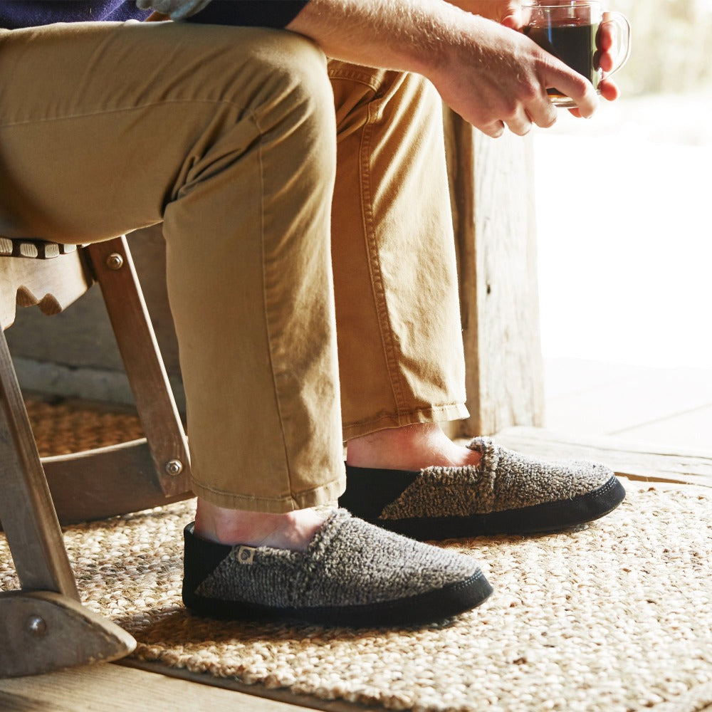Men’s Acorn Moc with Collapsible Heel Slipper in Earth Tex on figure. Man sitting in rocking chair near a doorway with a mug of coffee in his hands