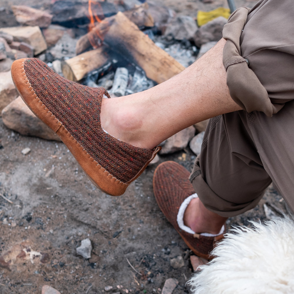 Men’s Sustainable Camden Moccasins on figure. Male model sitting with his legs crossed in front of a fire.