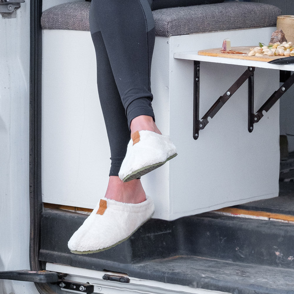 Women’s Algae-Infused Spa Slippers in Ewe on figure. Model sitting on seat in converted van with a charcuterie board next to her